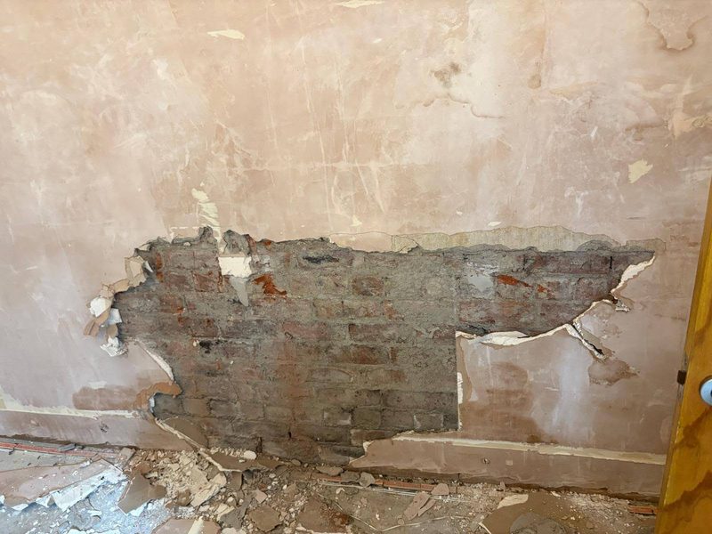 Blown plaster stripped back to reveal saturated, crumbling brickwork